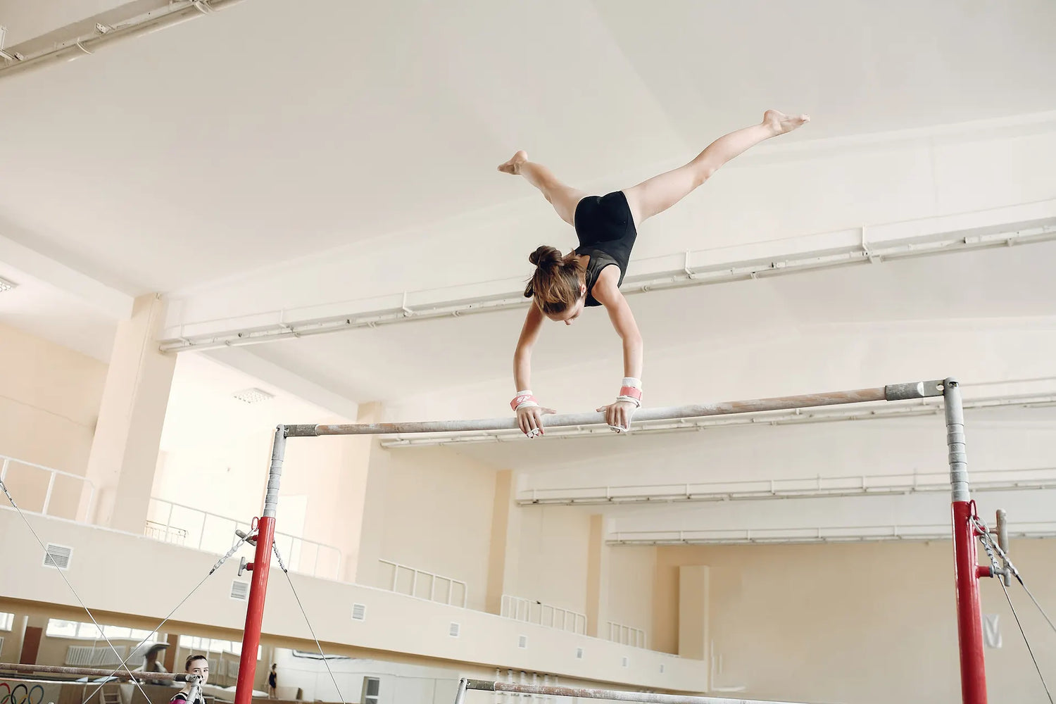 Ein Mädchen macht einen Handstand mit gegrätschten Beinen am oberen Stufenbarren-Holm. Dabei trägt sie Riemchen